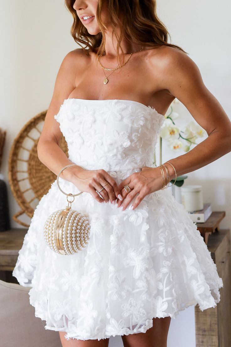 a woman wearing a white strapless dress and holding her hands on her hips while posing for the camera