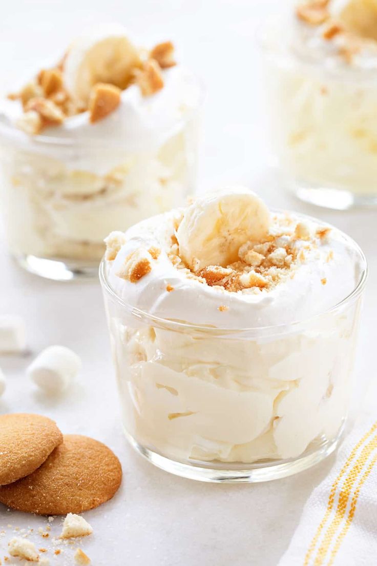 three desserts in small glass dishes with cookies on the side and one is topped with whipped cream