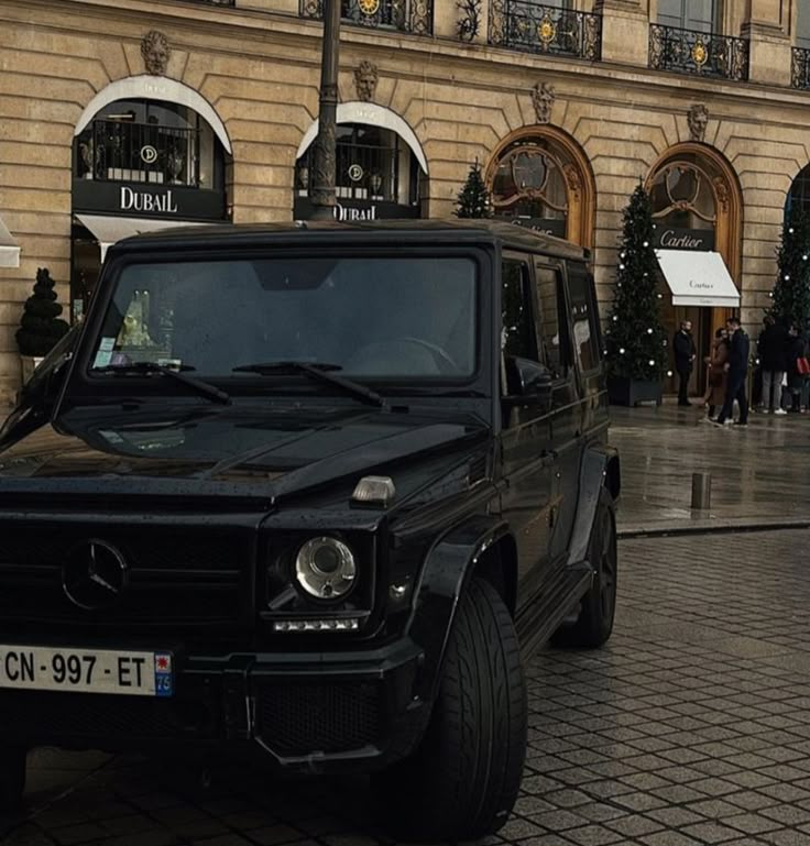 a black mercedes g class parked in front of a building with christmas decorations on it