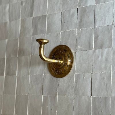 a gold hook on a white tiled wall