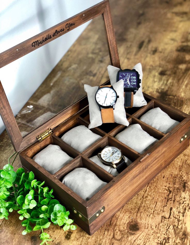 an open wooden watch box with six watches in it on a table next to some green plants