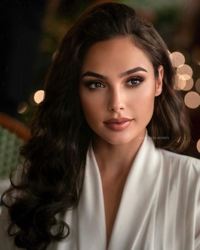 a woman with long black hair wearing a white shirt and posing for a photo in front of lights