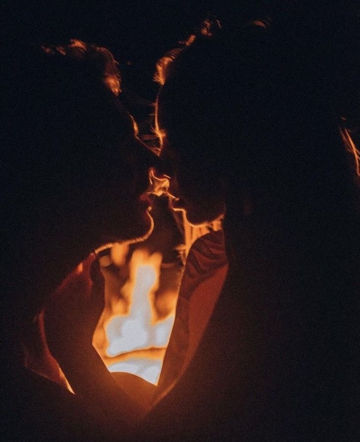 two people standing next to each other in front of a lit fire pit at night