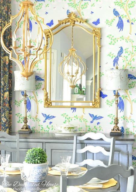 a dining room table with chairs and a mirror on the wall above it that is decorated in blue and gold