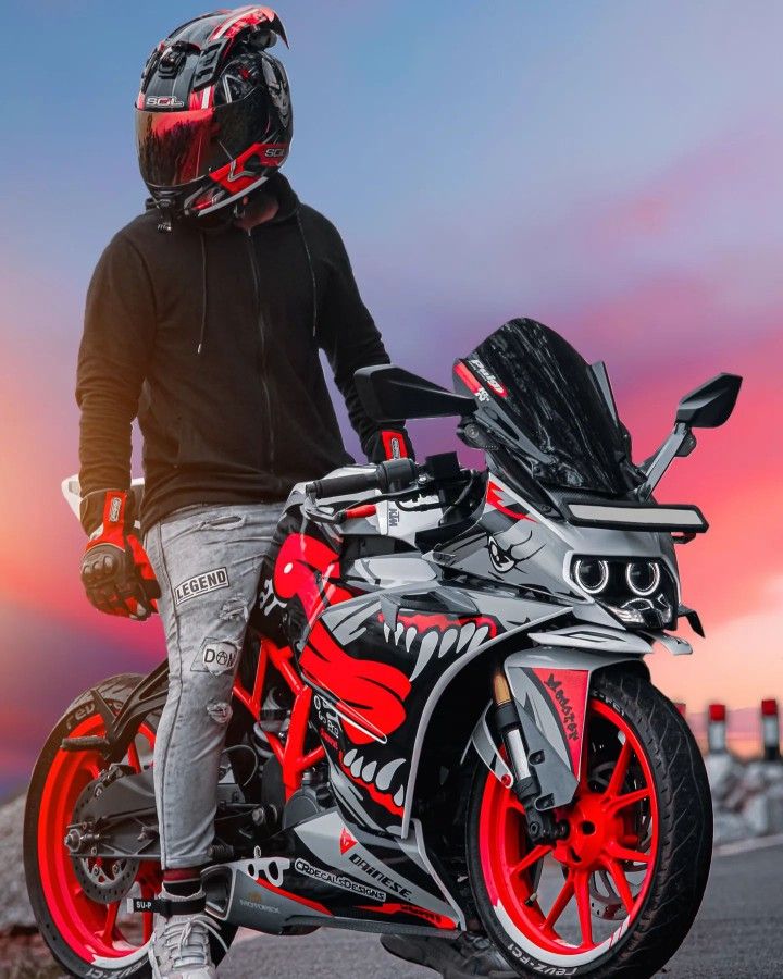 a man standing next to a red and black motorcycle with helmet on it's head