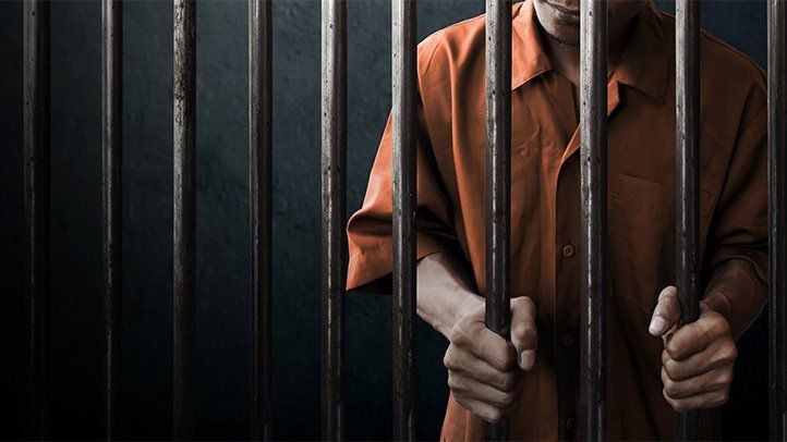 a man in an orange shirt is behind the bars of a jail cell, holding his hands out