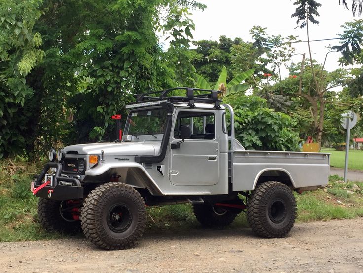 a silver truck parked on the side of a dirt road next to trees and bushes