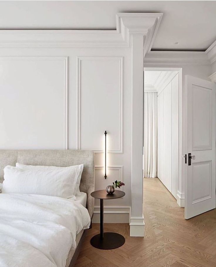 a bedroom with white walls and wood flooring is pictured in this image, there are two lamps on either side of the bed