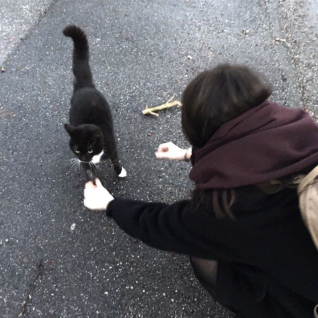 a woman kneeling down petting a black and white cat on the street next to a banana peel