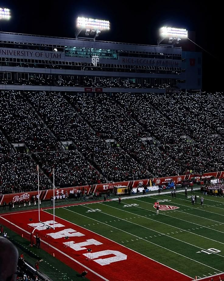 a football stadium filled with lots of people and lights on the sidelines at night