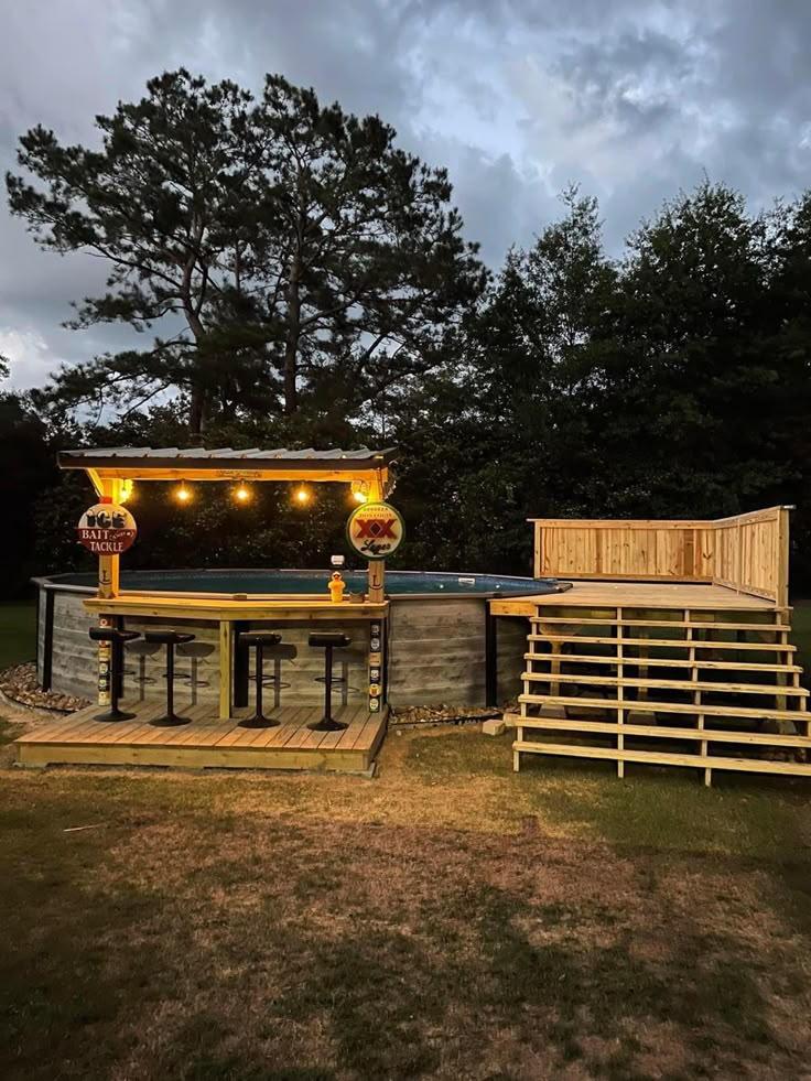 an outdoor bar with lights on the top and stairs leading up to it in front of trees