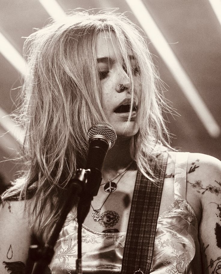 a black and white photo of a woman holding a guitar in front of a microphone