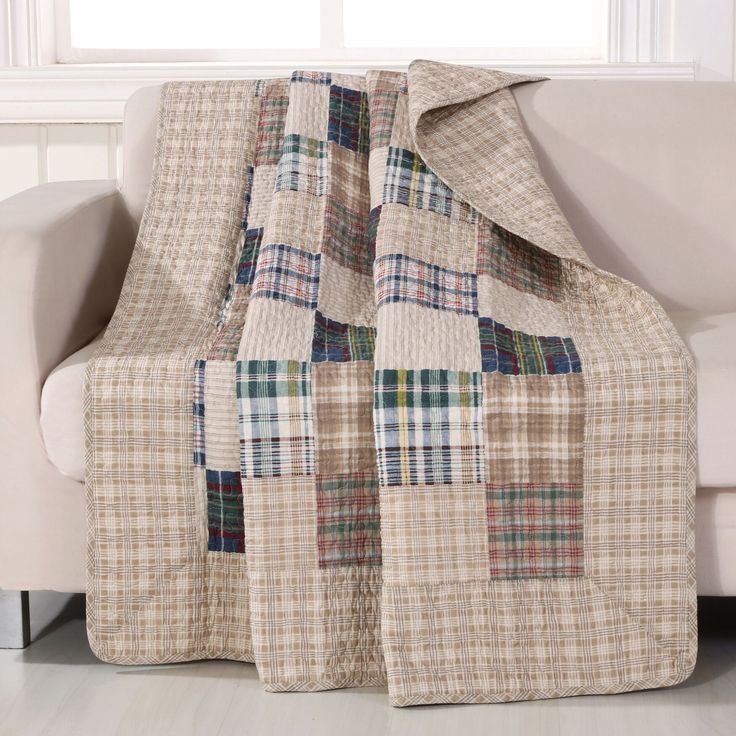 a couch with a plaid blanket on it next to a white chair and windowsill