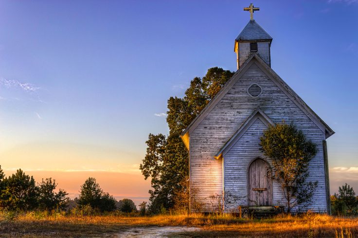 an old wooden church with a cross on the roof and steeple is shown at sunset