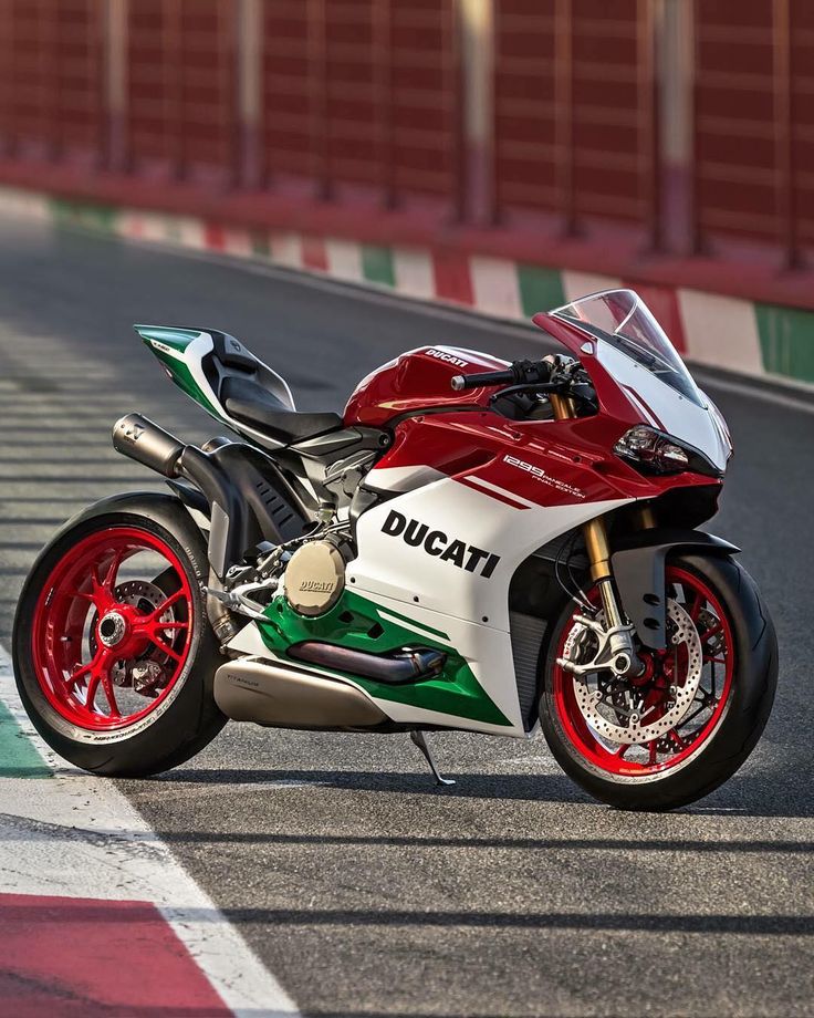 a red, white and green motorcycle parked on the side of a race track