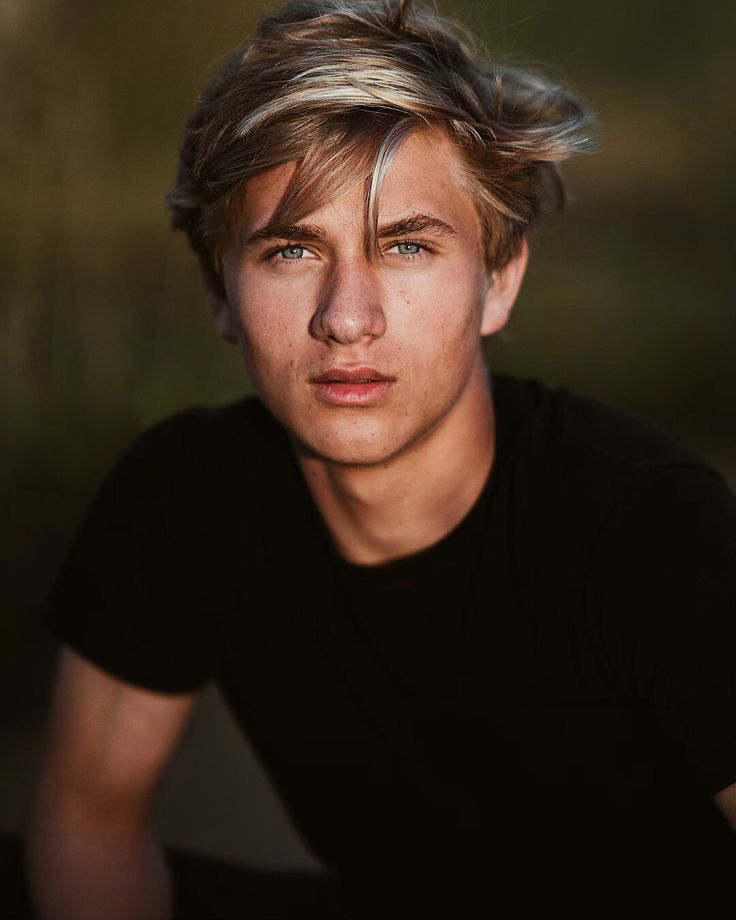 a young man with blonde hair is posing for a photo in front of a blurry background