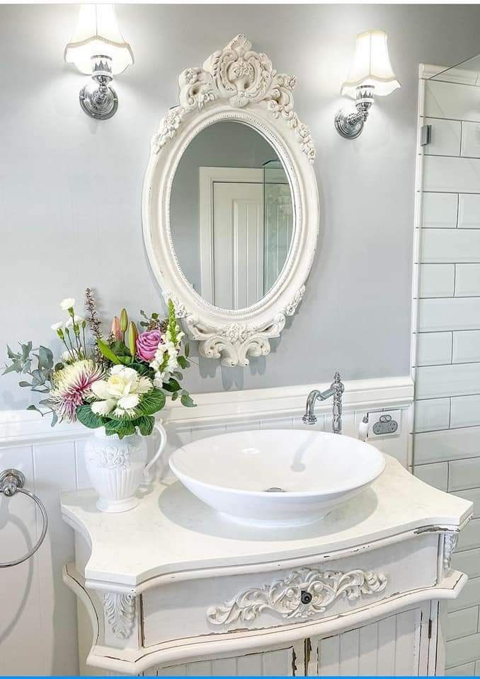 a white sink sitting under a bathroom mirror next to a vase with flowers in it