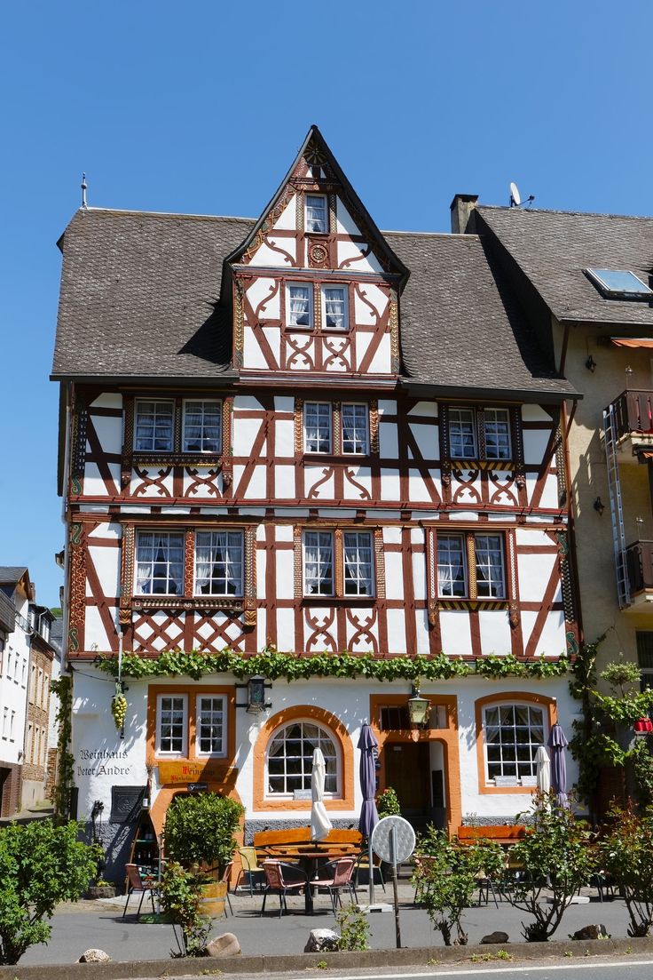 an old half - timbered building with tables and chairs on the outside, surrounded by greenery