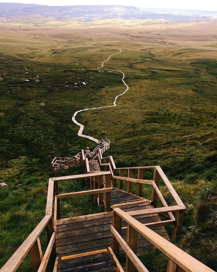 stairs lead down to the top of a grassy hill with rolling hills in the background