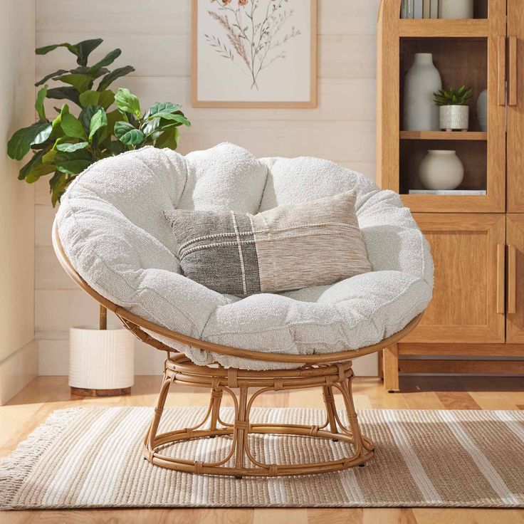 a chair with pillows on it in front of a bookcase and potted plant