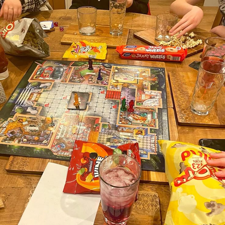 several people sitting at a table playing a board game with snacks and drinks on it