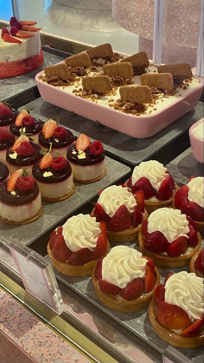 many different desserts are on display in a glass case at a bakery, including strawberries and cakes