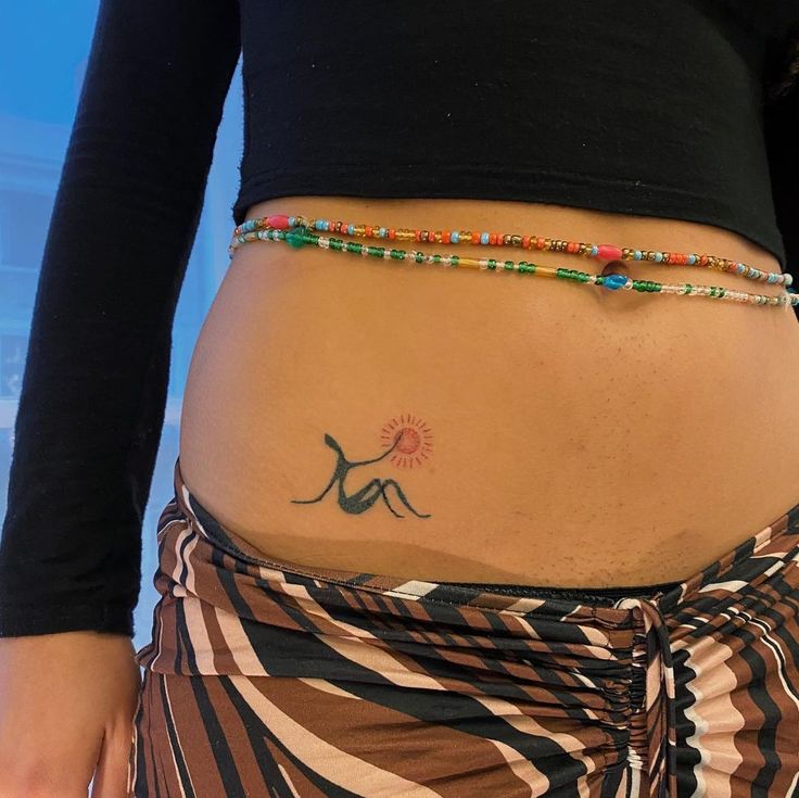 a woman's stomach with a tattoo on her belly and colorful beads around the waist