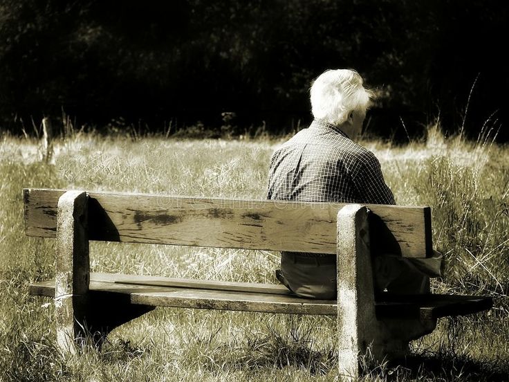 an old man sitting on a wooden bench in the middle of a field with tall grass