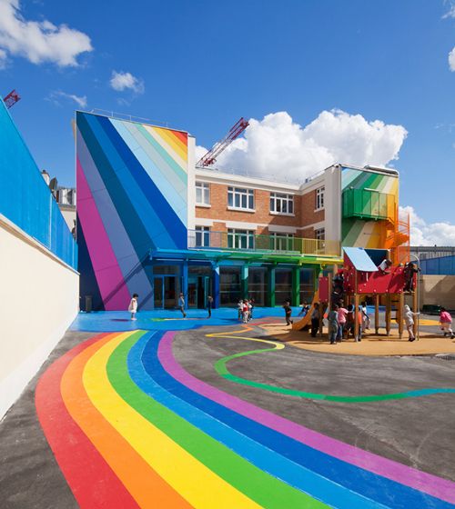 children play in front of colorful building with rainbow painted on the ground and people walking around