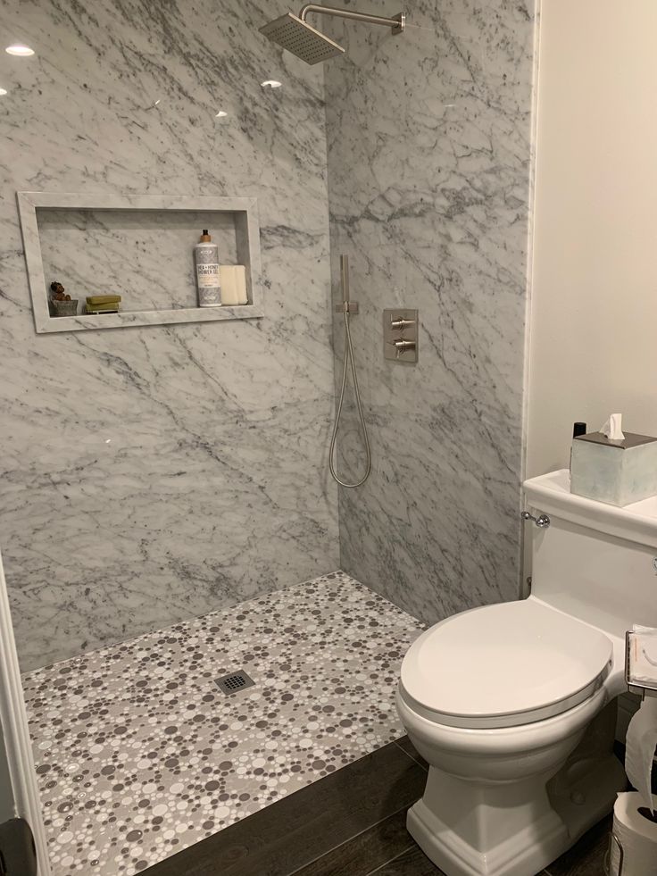 a white toilet sitting in a bathroom next to a walk in shower with marble walls