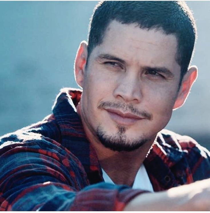 a close up of a person wearing a plaid shirt and looking at the camera with a serious look on his face