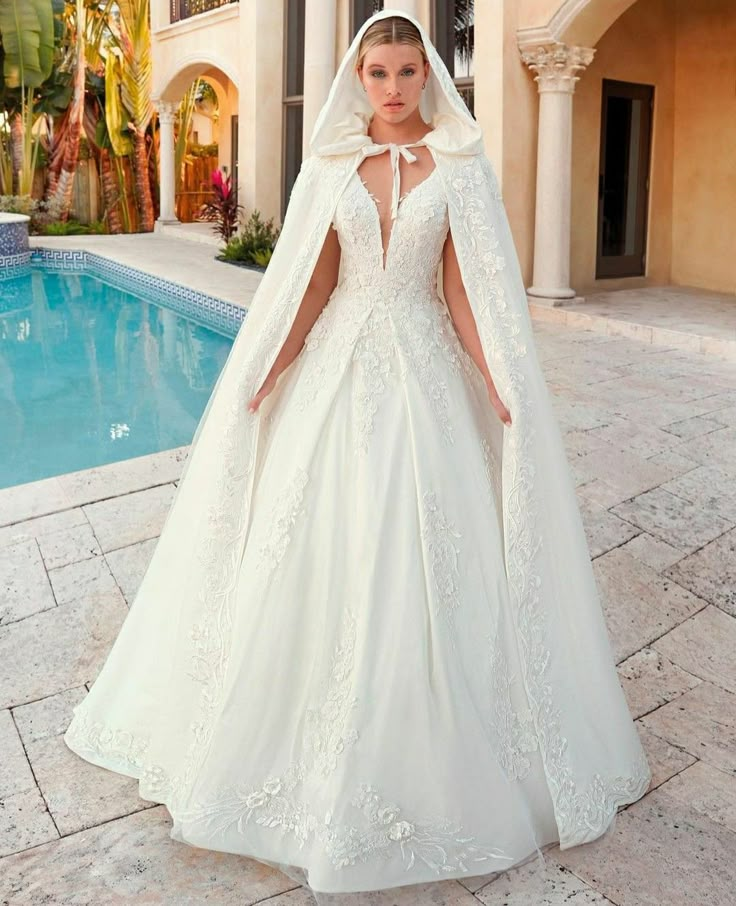 a woman standing in front of a swimming pool wearing a wedding dress and caped veil