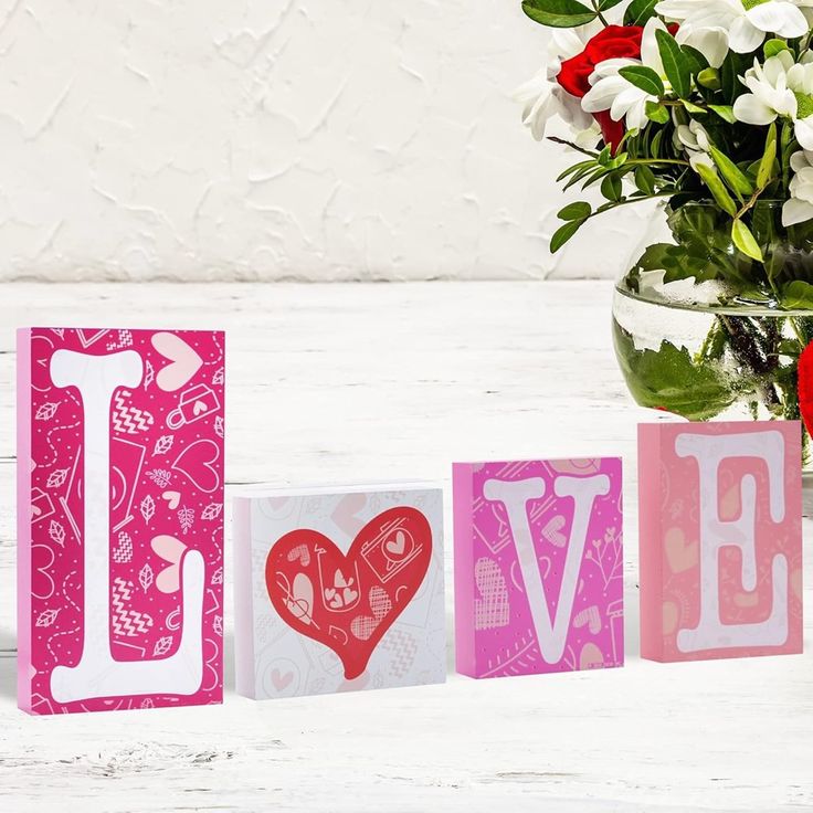 the word love spelled with wooden blocks in front of a vase filled with red and white flowers