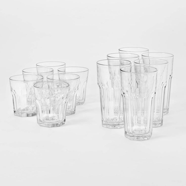 six clear glass tumblers lined up on a white surface with no one in them