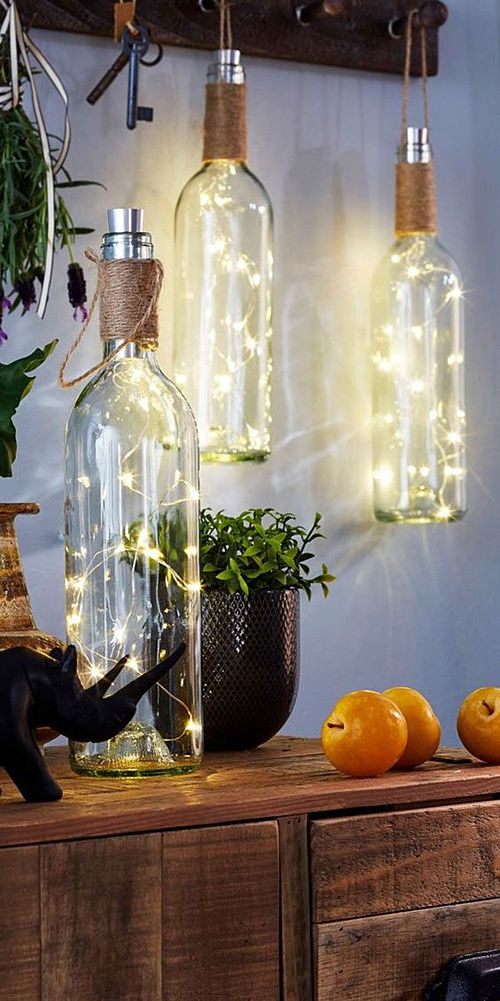 some bottles with lights in them are sitting on a table next to pumpkins and plants