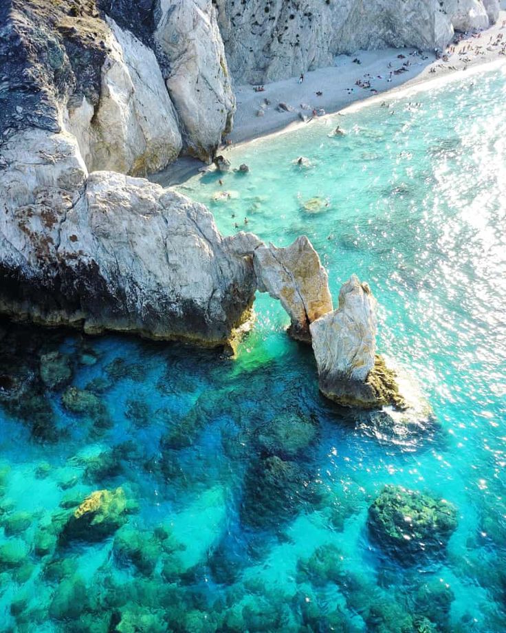 the water is crystal blue and clear with rocks on either side that are surrounded by green algae