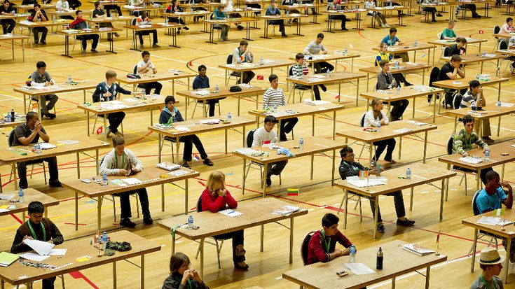 many students are sitting at desks in an empty room with one student writing and the other taking notes