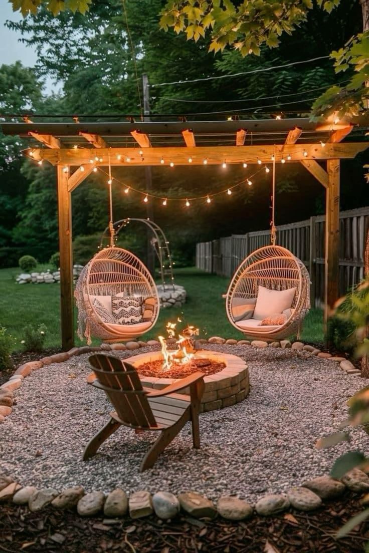 a patio with two hanging chairs and a fire pit in the middle, surrounded by gravel