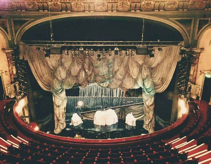 an empty theater with red seats and drapes on the curtained stage, looking down