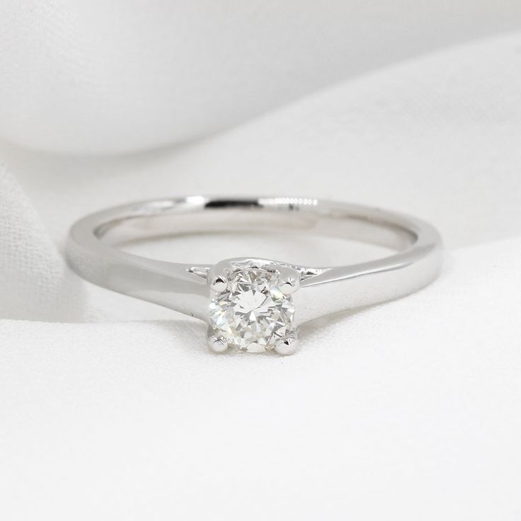 a diamond ring sitting on top of a white cloth covered tablecloth, with the center stone visible