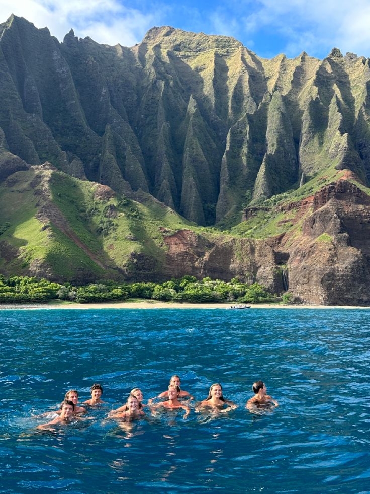 four people swimming in the ocean with mountains in the background