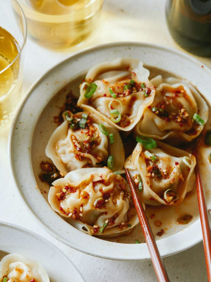 a white plate topped with dumplings and chopsticks next to two glasses of wine