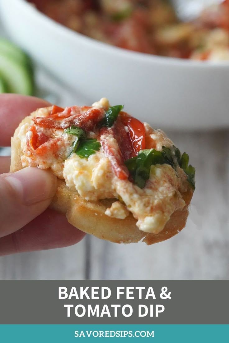 a hand holding up a piece of bread that has some food on it and the words baked feta and tomato dip