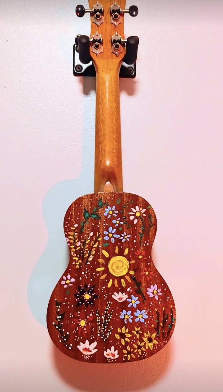 a wooden guitar hanging on the wall with flowers painted on it's back and sides