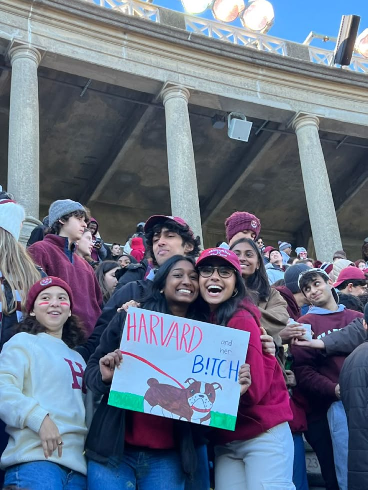 two girls hugging each other while holding a sign in front of an audience at a football game