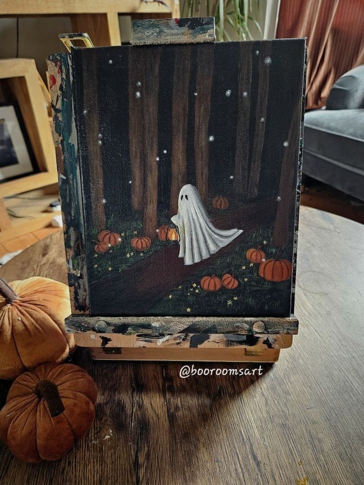 an easel with a painting of a ghost in the woods on it next to pumpkins