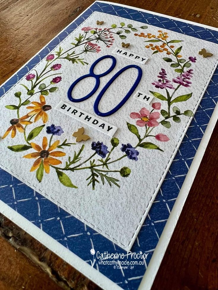 a birthday card with flowers and the number 80 on it's front, sitting on a wooden table