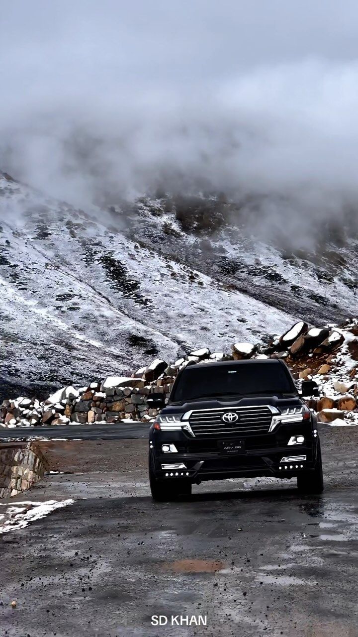 the black truck is driving down the road in front of some snow covered mountains and clouds