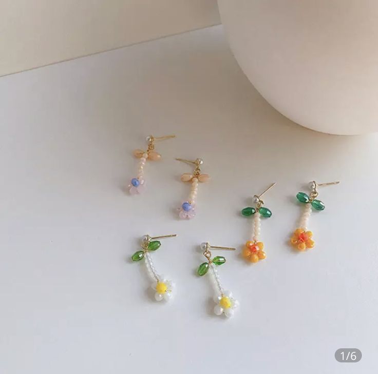 four pairs of earrings are sitting on a table next to a white vase with flowers in it