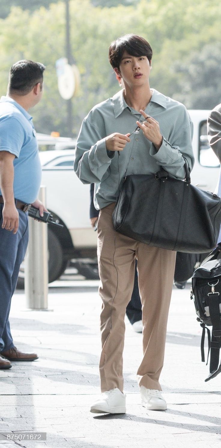 a man is walking down the street with his hand in his pocket and holding a black bag